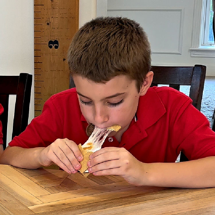 Image shows a kid eating a Smores with gooey marshmallows.