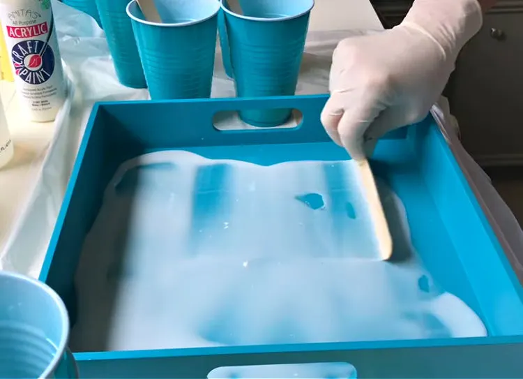 Spreading resin on a tray with a popsicle stick.