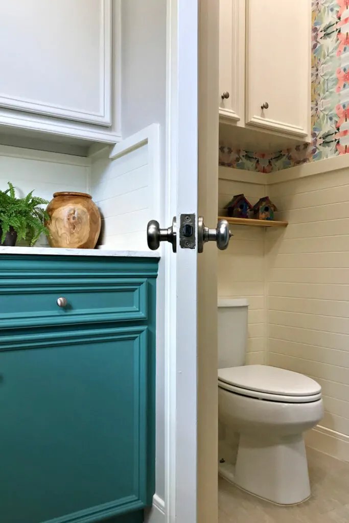 After photo of a colorful water closet with wainscoting and colorful wallpaper next to Laundry Room.