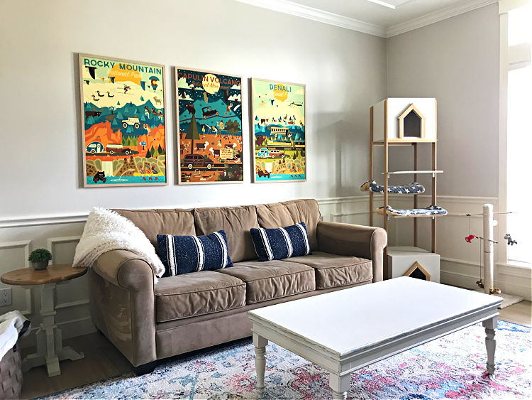 Image of an after picture of a before and after family room makeover post. Image shows a family room with a couch on a large rug with 3 vintage style posters above.