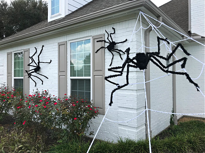 Image of white brick house with Giant Spider Halloween decorations. I LOVE this CHEAP & EASY Halloween theme on our house! Here's how to hang giant spider decorations outdoors with tons of photos to help you get the look.