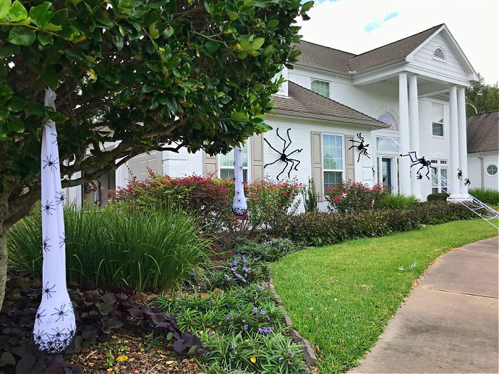 Image of white brick house with Giant Spider Halloween decorations. I LOVE this CHEAP & EASY Halloween theme on our house! Here's how to hang giant spider decorations outdoors with tons of photos to help you get the look.