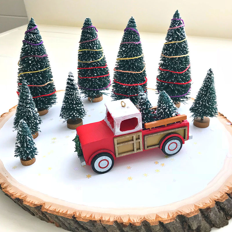 Image of a wood slice, vintage red truck Christmas ornament, and bottle brush trees used to make an easy DIY Red Truck Christmas decoration for a table or countertop.