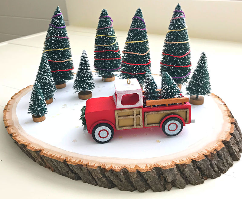 Image of a wood slice DIY Christmas decoration with a Red Truck ornament and bottle brush Christmas trees.