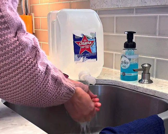 Image of a woman washing her hands with 2 1/2 gallon water container.