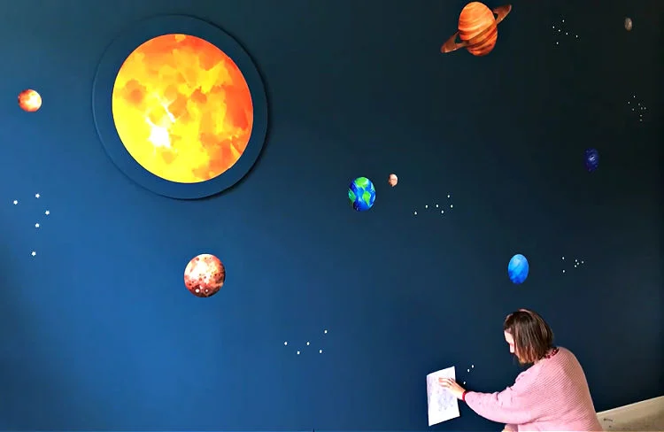 Image of someone using glow in the dark star stickers to make constellations and outer space.