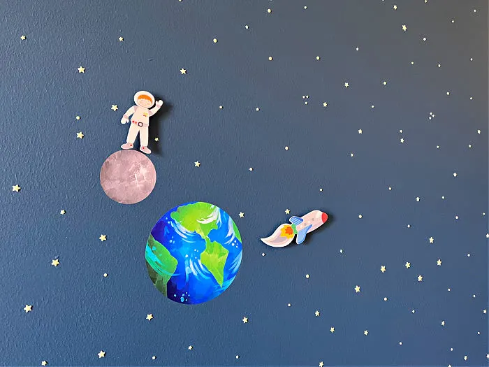 Image of a toy astronaut and rocket next to a vinyl sticker of Earth on an outer space boys bedroom wall.