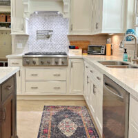 Image of a white kitchen with a blue rug for a post about where to put a kitchen sink and appliances when planning a kitchen.