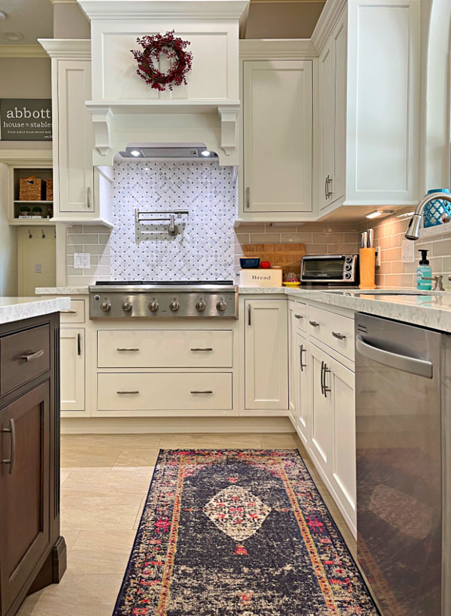 A large kitchen with white cabinets a large cabinet hood over a stainless steel gas stove with drawers beneath.