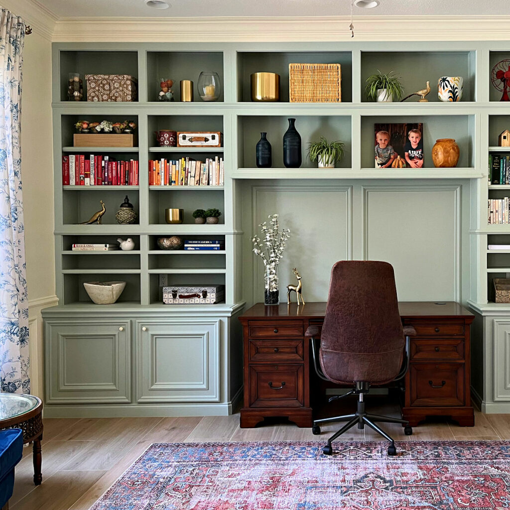 Image of a home office with floor to ceiling green built-in cabinets, a wood desk, tile floor, and a rug. After photo for a home office makeover.