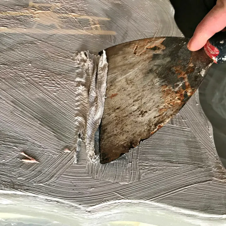 Image showing a paint scrapper removing citristrip from a table for a post about 5 ways to remove dried Citristrip on wood, furniture, concrete, and metal.