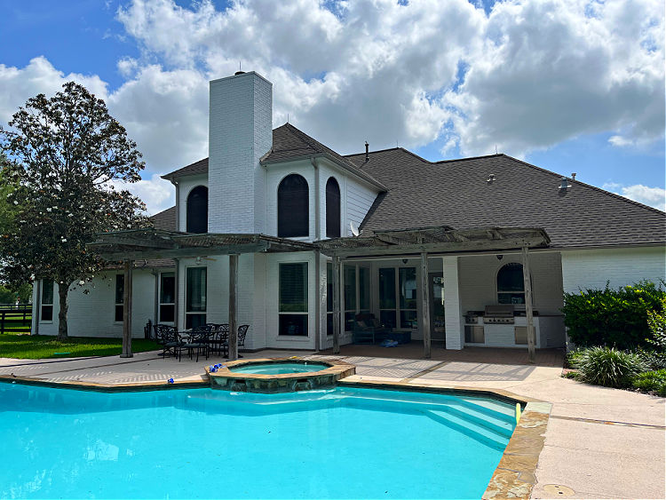 Large inground pool behind a white brick house.