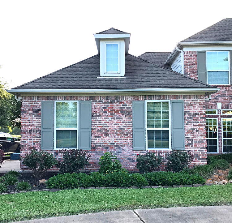 One side of the front of a brick house with medium brown shutters.