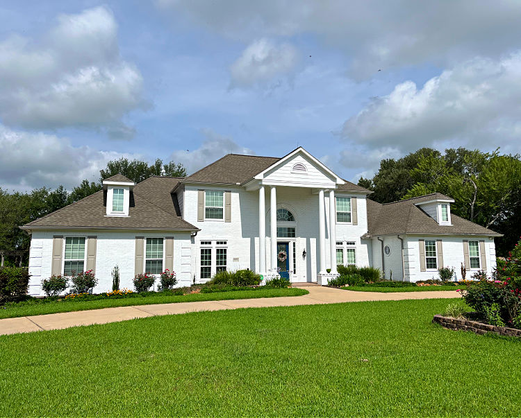 Large 2-story white brick house painted with Loxon XP with a big green grass yard.