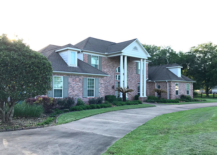 A red and grey brick house with white trim, white columns, and grey shutters.