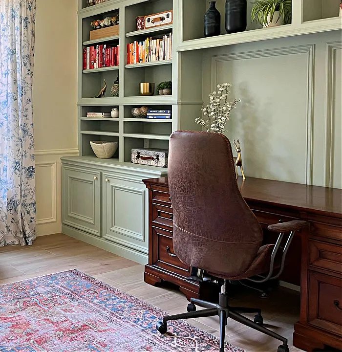 Home office with green built-in bookshelves and a brown faux leather office chair.