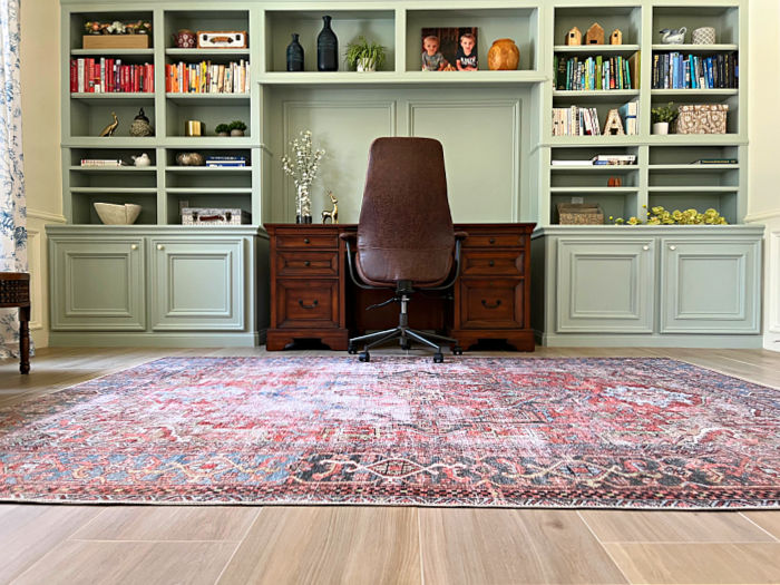 Home office with a large, traditional area rug on a faux wood tile floor, in front of built-ins.