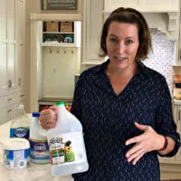 Image of someone holding white vinegar for a post about popular cleaners that damage your grout and floor tile.