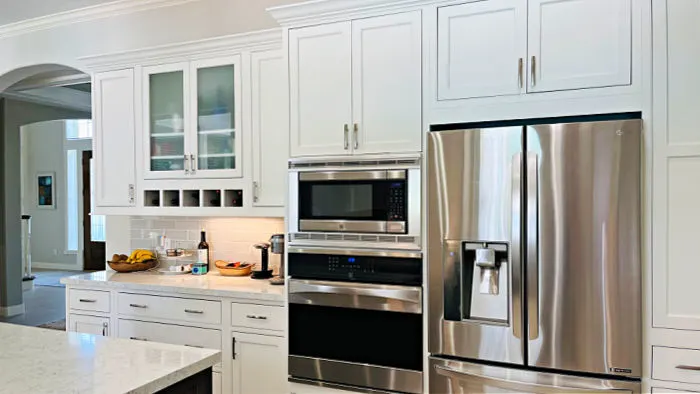 Stainless steel fridge, oven, microwave with white inset cabinets in a large kitchen.