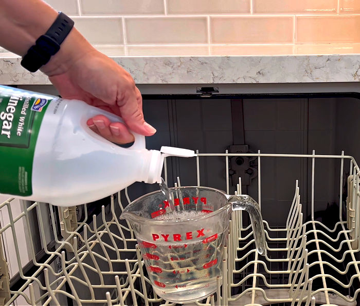 Image of vinegar in a cup on the top rack of a dishwasher. Vinegar used to clean the dishwasher.