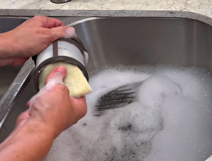 Using a scrub sponge to clean a dishwasher filter.