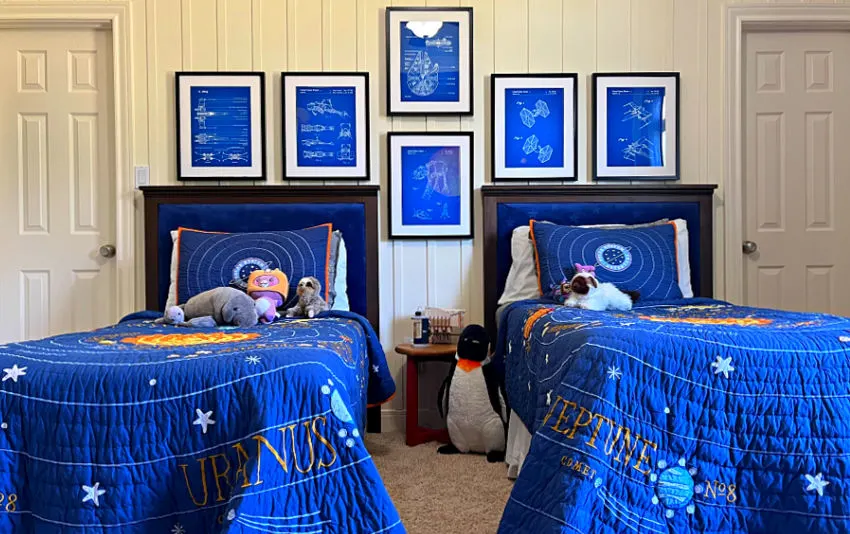 Solar System bedding from Pottery Barn on two twins bed in a boys shared bedroom with a white wall and Star Wars patent blueprint wall art.