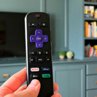 Image of a Roku remote in front of a TV for a post with the 11 Best Reasons to cut the cord with cable tv. With tips for how to ditch cable and why you should.
