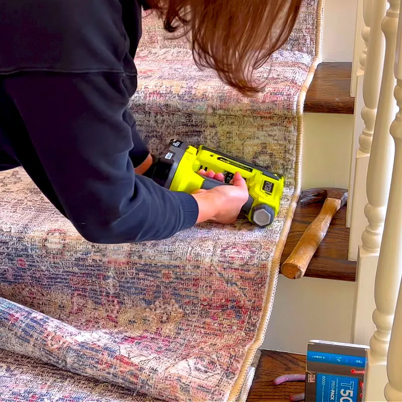 Using a Ryobi Crown Stapler to put a rug on stairs in a home.