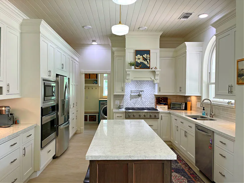 White cabinets in a kitchen with a stained wood island and white quartz counter tops. With a shiplap ceiling.