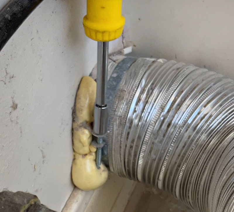 Using a socket to unscrew the strap on a dryer vent pipe.