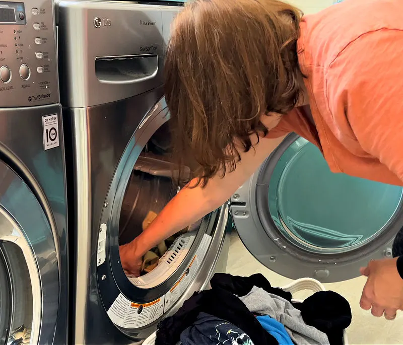 Someone removing clothes from a dryer for tips on what happens when you have a clogged dryer vent.
