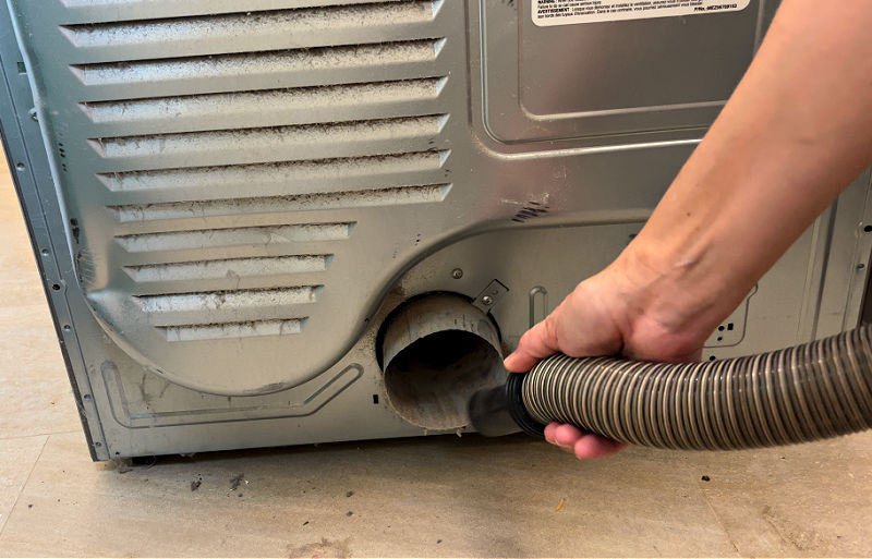 Cleaning the back of a dryer with brushes and a vacuum.