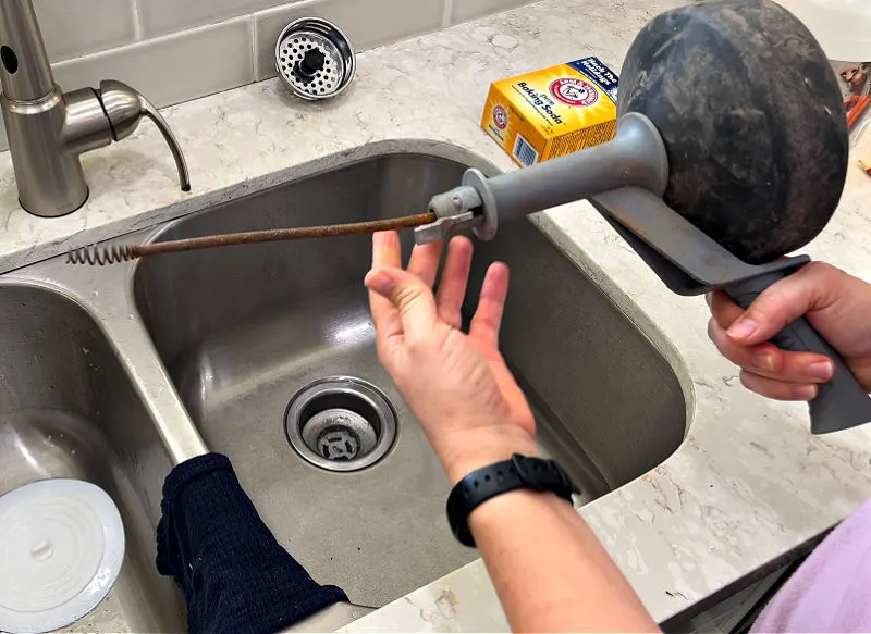Using an auger to clear a kitchen clogged sink drain.