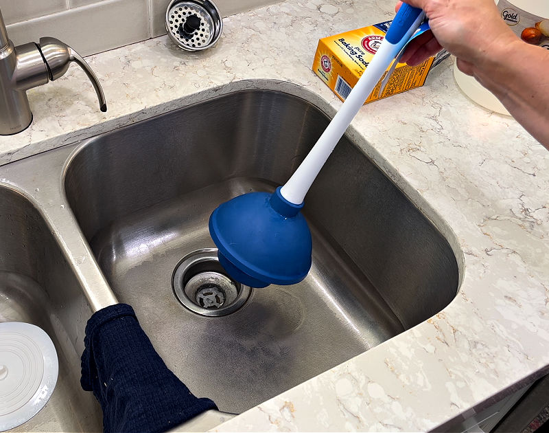 Using a plunger to clear a kitchen clogged sink drain.
